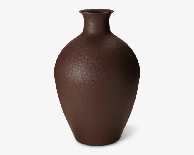 Høj, rund vase med en smal hals og udadgående kant, udført i en mat mørkebrun farve. Overfladen har en let tekstureret finish, hvilket giver et naturligt og jordnært udtryk. Vasen er uden dekorationer og fremhæver dens enkle og elegante form.
