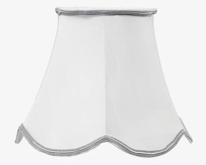 Hvid lampeskærm med udvidet, bølget bundkant og diskret sølvkant langs toppen og bunden. Stoffet har en let tekstur, hvilket giver et klassisk og elegant udtryk, der passer til traditionel eller vintage-inspireret indretning.