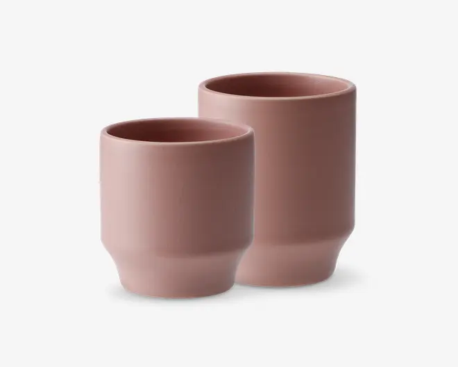 Sæt med to keramikkopper med mat finish i en afdæmpet rosa farve. Begge kopper har et moderne, minimalistisk design med glatte, lige sider og en let tilspidset bund. Sættet består af én højere og én lavere kop, begge uden hank og med et enkelt, stilrent udtryk.