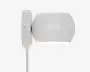 En moderne vægmonteret lampe med en glat, mat hvid overflade. Lampen har en rund, tromleformet skærm, der leder lyset nedad. Den er fastgjort til en rektangulær vægplade med en synlig skrue og har en hvid ledning, der går ud fra bunden. Designet er minimalistisk og passer godt til moderne indretning.