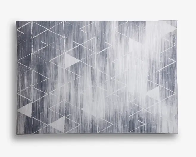 Rektangulært tæppe med et moderne geometrisk mønster af overlappende hvide trekanter og linjer på en grå baggrund med farveovergange. Designet har en børstet, let slidt effekt, hvilket giver et moderne og tekstureret udtryk. Kanterne er rene, og det samlede udseende er minimalistisk og stilfuldt.