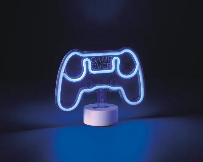 En dekorativ LED-lampe formet som en videospil-controller, oplyst med et blåt skær. Lampen har teksten 'GAME OVER' i midten og står på en rund, hvid base. Designet inkluderer konturer af knapper og joysticks, hvilket gør den velegnet til gaming-inspireret indretning.