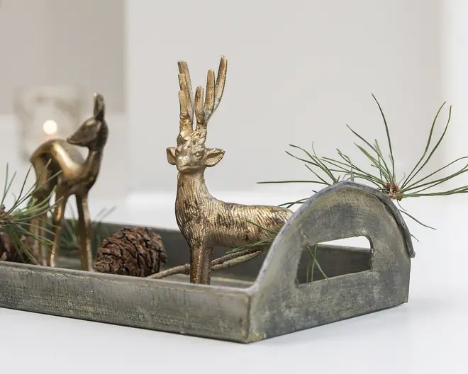 Rektangulært rustikt metalfad med buede håndtag, dekoreret med to gyldne hjortefigurer, fyrregrene og en kogle.