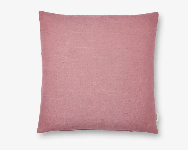 Firkantet pude med et blødt, støvet rosa betræk. Stoffet har en let vævet struktur, der giver en mat overflade. Kanterne er pænt syet, og der er et lille stofmærke i den ene side. Puden ser fyldig og komfortabel ud, velegnet til brug på sofa eller seng.
