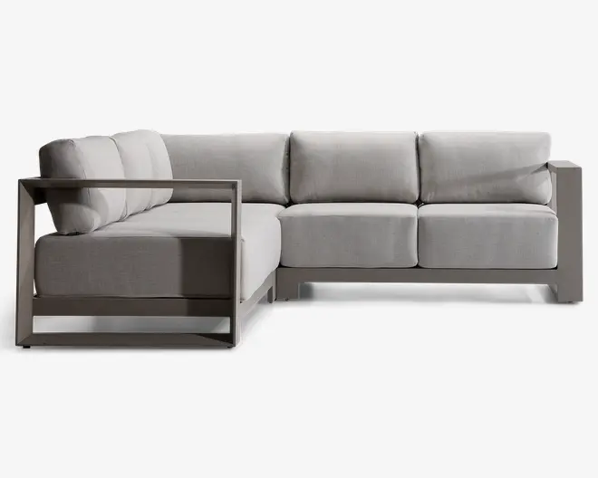 Moderne L-formet sofa med en robust, vinklet metalramme i mat finish. Sofaen har tykke, lysegrå hynder på både sæde og ryg, hvilket giver en blød og komfortabel siddeoplevelse. Armlænene er brede og firkantede, hvilket matcher rammestrukturen og det moderne design. Betrækket ser ud til at være lavet af et slidstærkt, vævet stof, velegnet til både indendørs og udendørs brug.