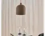 En mat brun kuppelformet pendellampe med en glat, afrundet top og en kort ophængningsledning, vist over et bord med glasplade foran bløde cremefarvede gardiner.