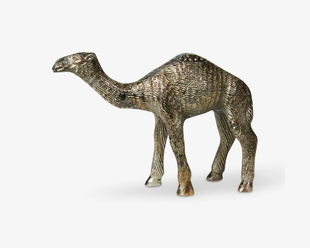 En metalfigur formet som en kamel med en tekstureret overflade, der efterligner pels, og realistiske detaljer som en tydelig pukkel, lang hals og slanke ben. Overfladen har en blanding af sølv- og bronzefarver, hvilket giver et antikt udseende.