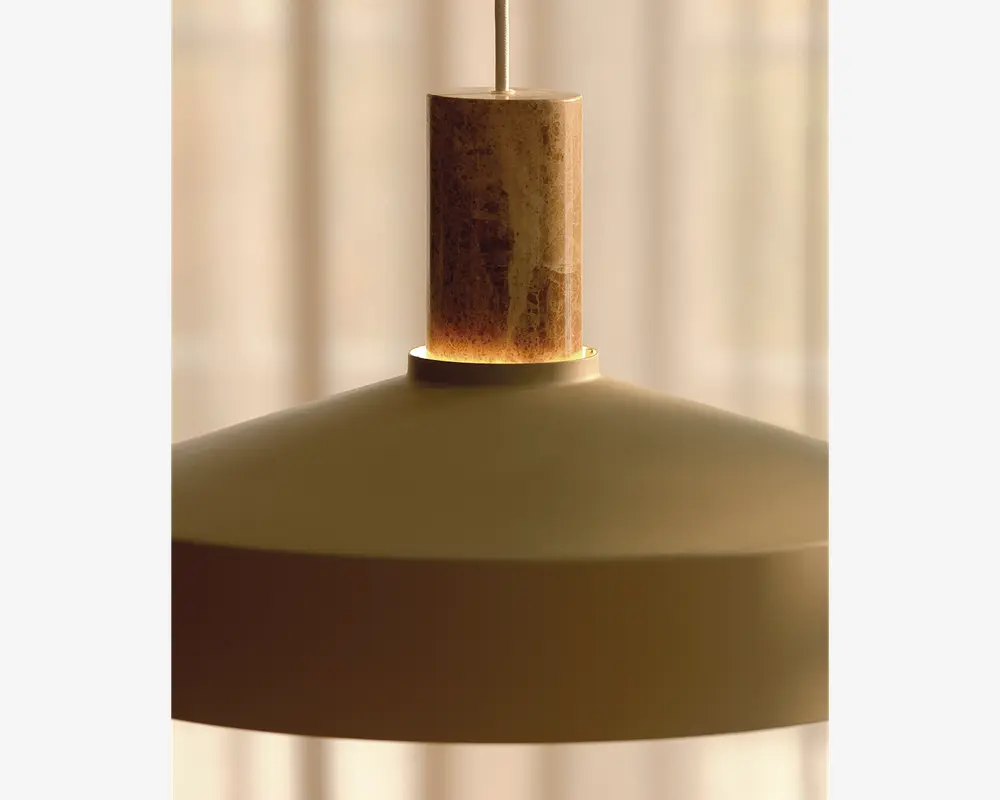 Nærbillede af en pendellampe med en glat, mat skærm i en afdæmpet beige eller taupe farve. Lampen har en cylindrisk topdel lavet af natursten eller marmor med synlige brune og lyse årer, hvilket giver et elegant og tekstureret udtryk. Designet er minimalistisk og moderne, velegnet til nutidige indretninger.