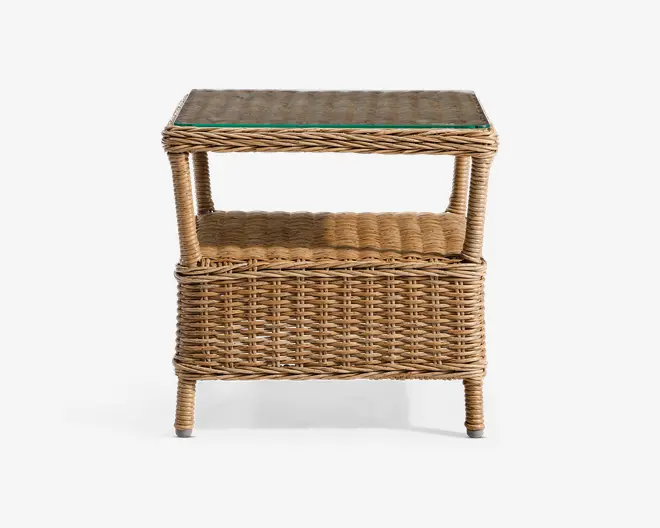 Rektangulært sidebord lavet af flettet rattan med naturlig finish. Bordet har en klar glasplade på toppen for en jævn overflade, en åben hylde nedenunder til ekstra opbevaring og solide ben med beskyttende ender. Designet inkluderer et nederste kurve-lignende rum, ideelt til organisering af ting. Bordet har et tekstureret, håndlavet udseende, egnet til både indendørs og udendørs brug.
