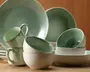Et sæt keramikservice med en blød grøn glasur på indersiden og en glat, offwhite yderside. Sættet indeholder store middagstallerkener, skåle og krus, alle med en diskret blank finish. Kanterne på krusene og skålene har en lidt mørkere grøn kant, som giver en flot kontrast. Delene har et moderne, minimalistisk design med blødt buede former, hvilket gør dem velegnede til både hverdags- og festbrug.