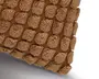 Nærbillede af brunt vævet stof dækket af små fluffy pompon-agtige totter, der viser en struktureret hjørnesøm mod hvid baggrund.