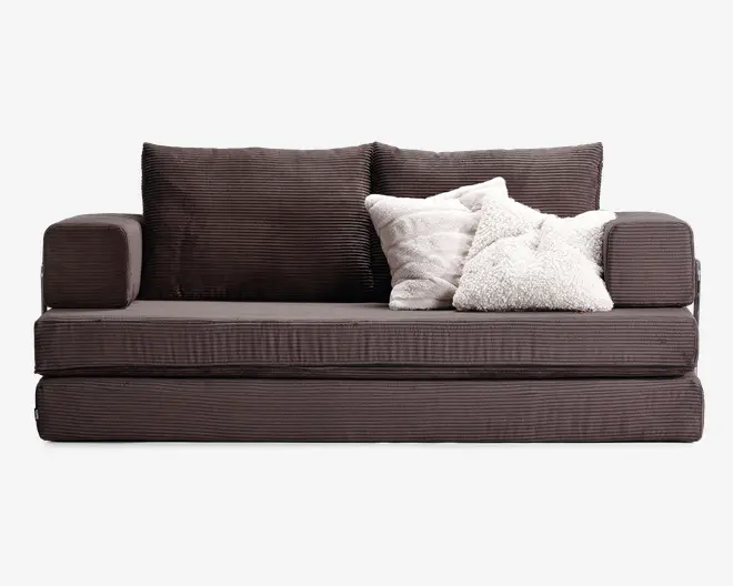 En moderne, kompakt sofa med mørkebrun fløjlstof og diskrete lodrette striber. Sofaen har to store, bløde ryghynder og to rektangulære armlæn. Sædet er tykt og velpolstret for ekstra komfort. Tre dekorative pyntepuder i forskellige hvide og cremefarvede nuancer, med forskellige teksturer—en fluffy, en quiltet og en glat—er arrangeret i højre side og giver et hyggeligt og indbydende udtryk.