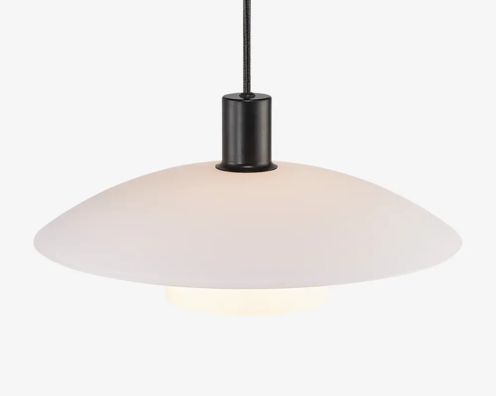 Hængelampe med en bred, lav, mat hvid skærm med glat overflade. Skærmen er fastgjort til en sort cylindrisk fatning og hænger fra en sort ledning. Lyskilden er skjult under skærmen og giver et blødt, diffust lys.