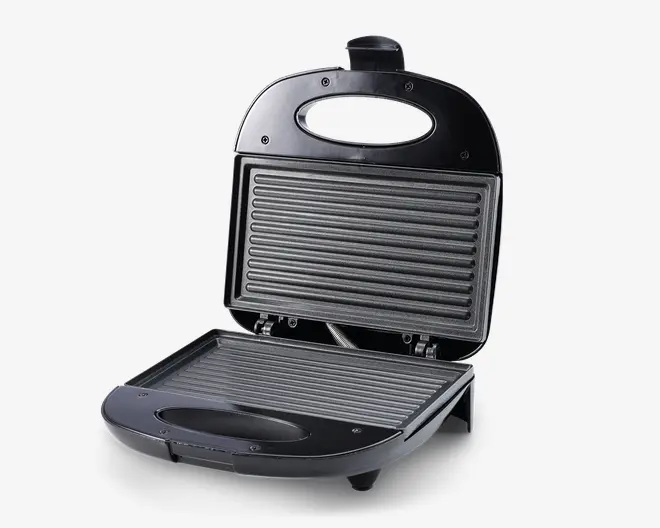 En kompakt elektrisk grill med sort plastydre og håndtag øverst. Grillen har to non-stick, riflede grillplader, der sikrer jævn tilberedning og nem rengøring. Pladerne er rummelige nok til sandwiches eller panini, og apparatet har en solid base med små fødder for stabilitet.