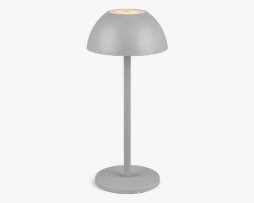 Moderne bordlampe med mat lysegrå finish. Lampen har en kuppelformet skærm, en lige cylindrisk stang og en rund, flad fod. Lampen udsender et blødt, varmt lys fra åbningen i toppen af skærmen, hvilket skaber en diskret glød. Minimalistisk design, der passer til moderne indretning.