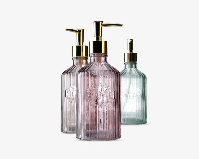 Tre elegante pumpeflasker i glas med lodret rillet struktur og præget 'SOAP'-mærke på forsiden. Hver flaske har en diskret farvetone: én er lyserød, én er klar, og én er lysegrøn. Alle har blanke guldfarvede pumpetoppe, hvilket giver et stilfuldt og luksuriøst udtryk.