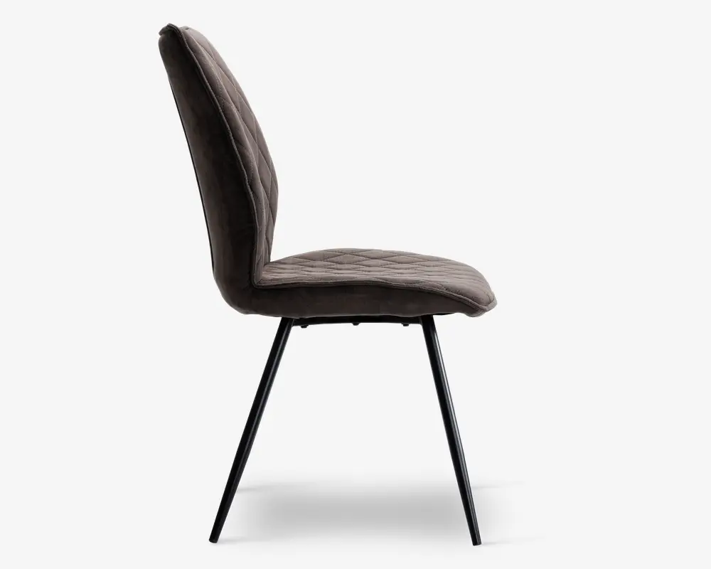 Sidebillede af en stol med blødt, mørkt polstret sæde og ryglæn med diskrete lodrette syninger. Stolen har et let buet ryglæn for ergonomisk støtte og står på fire slanke, skråtstillede metalben med mat sort finish.