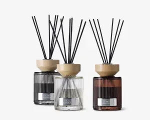 Sæt med tre duftpinde i riflede glasbeholdere, hver i en forskellig farve: sort, klar og ravfarvet. Hver diffuser har et lyst trælåg og flere sorte pinde til at sprede duften. Beholderne har et moderne, elegant design med en metallabel på forsiden.