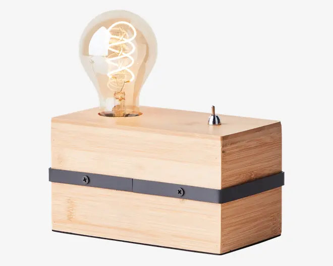 En rektangulær lampefod i lyst træ med en synlig sort metalbånd, der er fastgjort med skruer omkring midten. Ovenpå sidder en stor, synlig Edison-pære med spiralformet glødetråd samt en lille, metallisk vippekontakt ved siden af pæren. Designet er minimalistisk og industrielt med fokus på træets årer og pærens retro-udtryk.