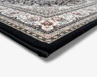 Nærbillede af et tæppehjørne, der viser en tyk, blød luv med et detaljeret, indviklet mønster. Kanten har udsmykkede blomster- og geometriske designs i nuancer af creme, blå, rød og guld, sat mod en ensfarvet sort kant. Tæppet fremstår veludført med tæt vævede fibre og en blød, luksuriøs tekstur.