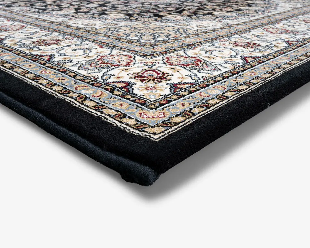 Nærbillede af et tæppehjørne, der viser en tyk, blød luv med et detaljeret, indviklet mønster. Kanten har udsmykkede blomster- og geometriske designs i nuancer af creme, blå, rød og guld, sat mod en ensfarvet sort kant. Tæppet fremstår veludført med tæt vævede fibre og en blød, luksuriøs tekstur.