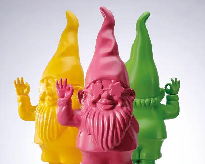 Tre dekorative nissefigurer med blank overflade, hver i en klar farve: gul, pink og grøn. Nisserne har lange skæg, høje spidse huer og laver sjove håndtegn—en med et peace-tegn, en der vinker, og en der laver et 'OK'-tegn. Den pink nisse foran har solbriller formet som stjerner, hvilket giver et legende udtryk.