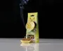 Billedet viser et sæt røgelseskegler med en citroninspireret keramisk holder og et matchende ornament formet som en citronskive. Røgelseskeglerne er placeret i holderen, hvoraf én kegle brænder og udsender en tydelig røgstribe. Emballagen står oprejst og har et vindue, der viser keglerne indeni, og citronskive-ornamentet er fastgjort på forsiden. Det samlede design fremhæver et frisk citrus-tema med gule og grønne farver.