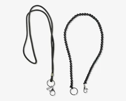 To forskellige sorte snore vises. Den til venstre er lavet af en glat, rund snor med en metal karabinhage og ring i enden, velegnet til at fastgøre nøgler eller små tilbehør. Den til højre har et flettet design, også sort, med en tykkere tekstur og udstyret med en metal karabinhage og ring for sikker fastgørelse. Begge snore har et enkelt og funktionelt udseende.
