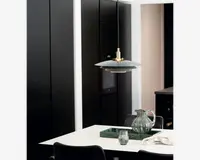 En moderne pendellampe med en flad, cirkulær skærm i mat grå, ophængt fra en sort ledning. Lampen har en messingdetalje øverst, hvor ledningen møder skærmen, hvilket giver et elegant udtryk. Skærmen er designet til at lede lyset nedad og giver målrettet belysning til området under lampen.