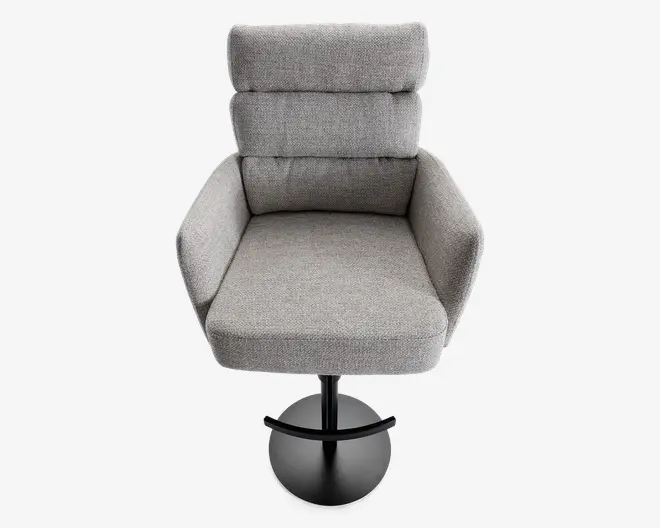 Moderne lænestol med høj, segmenteret ryg og bred, polstret sæde. Betrukket med lysegråt stof med blød, tekstureret overflade. Har skrå armlæn og en solid, rund sort metalsokkel, der giver stabilitet og nem rotation.