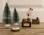Billedet viser en samling af små juledekorationer arrangeret på en træoverflade. Der er to grønne juletræer lavet af flaskerensere med hvide fodder, en lille brun kasse med to brune hundehvalpefigurer og et skilt, hvor der står 'glædelig jul', en lille værktøjskasse med mærket 'TOOLS', der indeholder miniatureværktøj, samt en lille stegepande med et spejlæg. I baggrunden er der en slikstok med et skilt, hvor der står 'Santa's workshop', som er sat op på væggen.