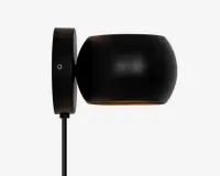 Væghængt lampe i mat sort med en rund, trommeformet lampeskærm. Lampen har en glat overflade og en diskret metallisk finish. Lyset rettes nedad, og lampen er monteret på en cirkulær vægplade med en synlig skrue. En sort ledning går ud fra bunden af vægpladen.