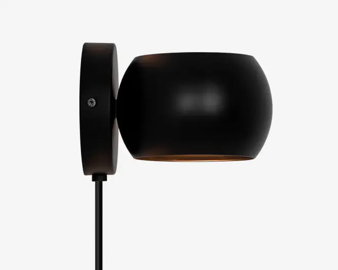 Væghængt lampe i mat sort med en rund, trommeformet lampeskærm. Lampen har en glat overflade og en diskret metallisk finish. Lyset rettes nedad, og lampen er monteret på en cirkulær vægplade med en synlig skrue. En sort ledning går ud fra bunden af vægpladen.