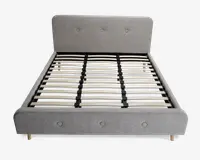 En moderne sengeramme med lysegråt polstret hovedgærde og fodgærde, begge med knapdetaljer. Rammen har lameller af træ til at støtte madrassen og står på korte, lyse træben. Designet er minimalistisk og nutidigt med rene linjer og en blød tekstiloverflade.