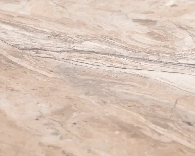 Nærbillede af en overflade med beige og lysebrun marmormønster. Teksturen har naturlige, snoede årer og diskrete farvevariationer, hvilket giver et elegant og organisk udseende. Overfladen ser glat og poleret ud, velegnet til bordplader eller gulve.