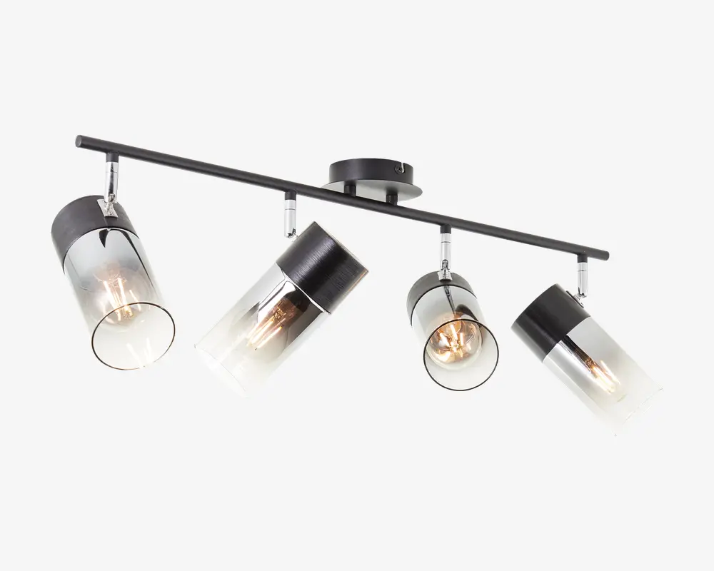Moderne loftlampe med fire justerbare cylindriske spotlys. Hvert spotlys har en sort metalbase og en klar glasafskærmning, så pærerne er synlige. Lampen er monteret på en lige sort metalstang, der er fastgjort til en rund loftsroset. Designet er stilrent og moderne, velegnet til retningsbestemt belysning i stue eller køkken.