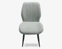 Stol med lysegråt polstret sæde og ryglæn, der har lodrette syninger på ryglænet for ekstra struktur. Sædet er bredt og afrundet, mens ryglænet er let tilspidset foroven. Stolen står på fire slanke, sorte metalben, der er let skråtstillede for stabilitet.