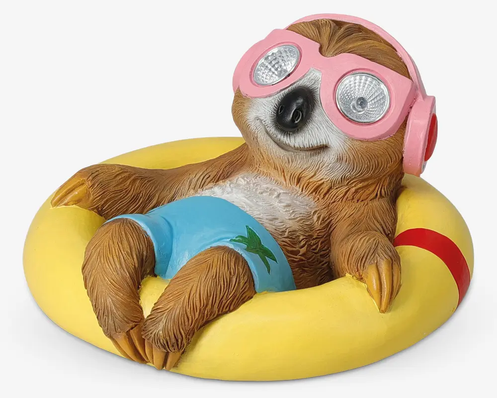En dekorativ figur af en afslappet dovendyr, der ligger i en gul badering. Dovendyret har blå badebukser med et grønt palmetræsmotiv og store lyserøde svømmebriller med reflekterende linser. Figuren har detaljeret pelsstruktur og et glad ansigtsudtryk.