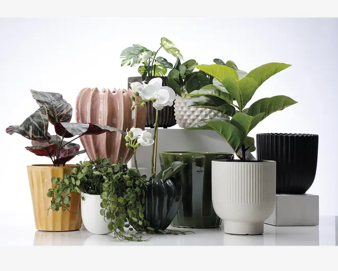 Et udvalg af dekorative urtepotter i forskellige former, størrelser og farver er udstillet sammen. Potterne har unikke teksturer såsom riflede, rillede og facetterede overflader og fås i nuancer af gul, lyserød, grøn, hvid, sort og mørkegrøn. Nogle potter har en blank finish, mens andre er matte. Opsætningen viser potterne både med og uden planter og fremhæver deres design og alsidighed til boligindretning.