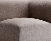 Nærbillede af et møbel betrukket med et tekstureret, taupefarvet stof. Billedet fremhæver det glatte, afrundede sæde og den tykke, støttende ryglæn, begge med rene, moderne linjer og en blød, behagelig overflade.