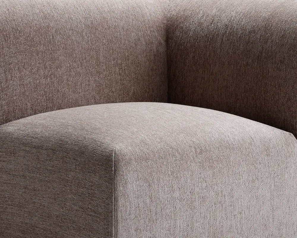 Nærbillede af et møbel betrukket med et tekstureret, taupefarvet stof. Billedet fremhæver det glatte, afrundede sæde og den tykke, støttende ryglæn, begge med rene, moderne linjer og en blød, behagelig overflade.