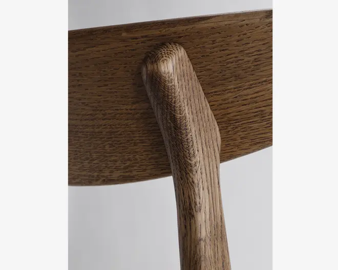 Nærbillede af ryglænet og støtten på en træstol, der fremhæver de glatte, afrundede kanter og den naturlige træstruktur. Håndværket viser sømløse samlinger og en varm, mellembrun bejdse, som fremhæver træets tekstur og kvalitet.