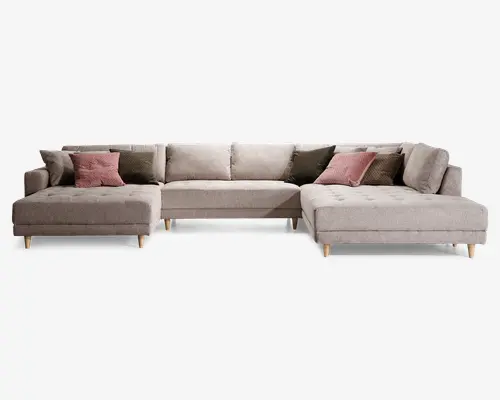 Stor L-formet sofa med lyse beige betræk og knapdetaljer på sædehynderne. Sofaen har brede, dybe siddepladser og lave ryglæn med flere løse ryghynder for ekstra komfort. Udstyret med koniske ben i træ og leveres med pyntepuder i støvede rosa og olivengrønne nuancer for ekstra stil og støtte.