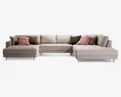 Stor L-formet sofa med lyse beige betræk og knapdetaljer på sædehynderne. Sofaen har brede, dybe siddepladser og lave ryglæn med flere løse ryghynder for ekstra komfort. Udstyret med koniske ben i træ og leveres med pyntepuder i støvede rosa og olivengrønne nuancer for ekstra stil og støtte.