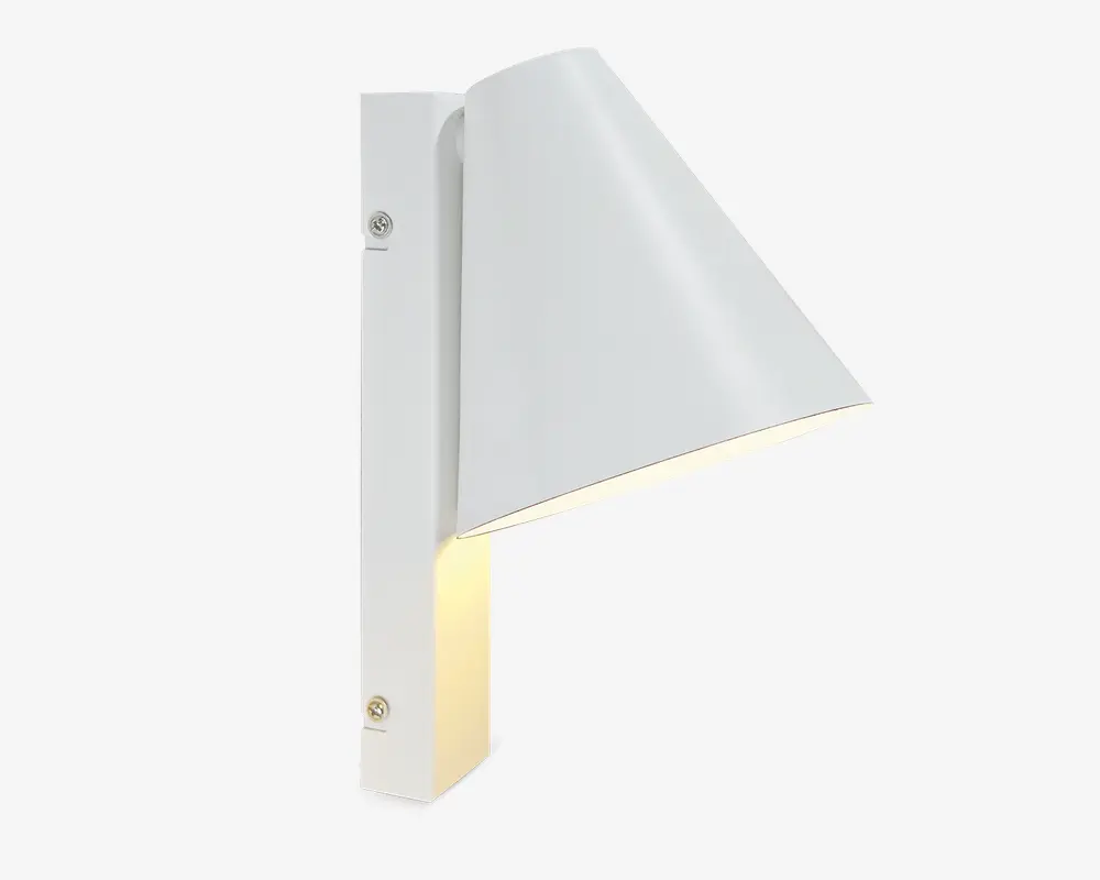 En moderne vægmonteret lampe med mat hvid finish. Designet har en lodret, rektangulær base med to synlige monteringsskruer og en konisk skærm, der leder lyset nedad. Skærmen er vinklet væk fra væggen og giver fokuseret belysning nedenunder. Lampen har rene linjer og et minimalistisk udtryk, der passer til moderne indretning.