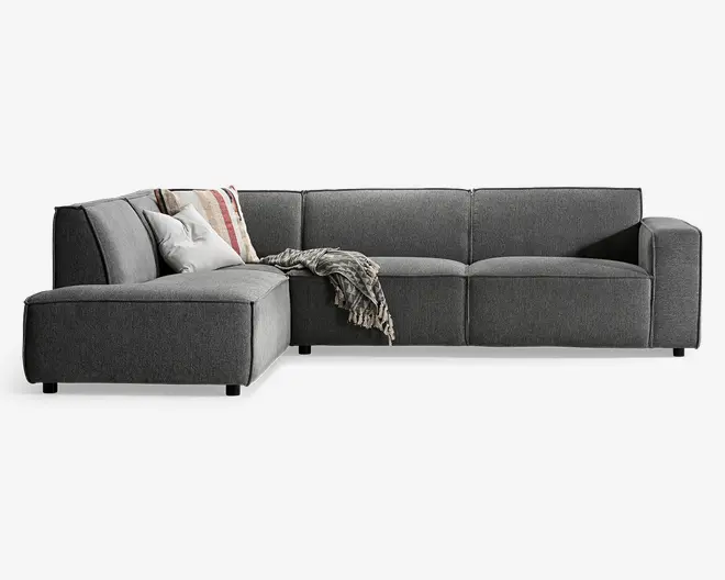 Moderne L-formet hjørnesofa betrukket med mørkegråt stof, med rene linjer og brede armlæn. Sofaen består af tre siddepladser og en chaiselong til venstre. Den er pyntet med to dekorative puder – én ensfarvet lysegrå og én med stribet mønster – samt et tekstureret tæppe, der er lagt over hjørnet. Sofaen står på korte, solide ben og giver et moderne og komfortabelt siddevalg.