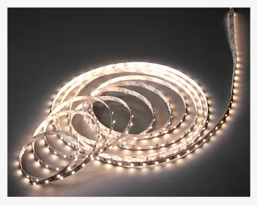 Fleksibel LED-lysbånd med jævnt fordelte, klare hvide lys langs hele længden. Båndet er rullet sammen i flere løkker, hvilket viser dets fleksibilitet og evne til at formes efter behov. Overfladen på båndet er glat og har et gennemsigtigt lag over LED'erne for beskyttelse. Bagsiden har sandsynligvis klæbemiddel for nem montering på forskellige overflader.