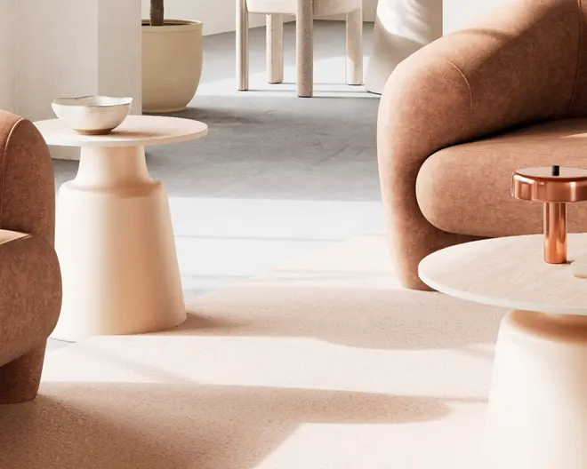 Billedet viser en moderne stue med bløde, afrundede møbler i neutrale beige og lysebrune nuancer. Lænestole og sofaer har polstrede, buede armlæn og en glat stoftekstur. Der er to sideborde med et minimalistisk, cylindrisk design og mat finish; det ene har en lille dekorativ skål, og det andet en metallisk lysestage. Gulvet er dækket af et lyst, tekstureret tæppe, og i baggrunden ses en stor plantekrukke samt et spiseområde med matchende lyse stole. Stilen er moderne og hyggelig med fokus på komfort og enkelhed.