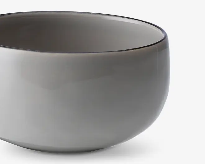 En rund skål med glat overflade og blank, lysegrå yderside og inderside. Skålen har et enkelt, minimalistisk design uden synlige mønstre, hanke eller dekorationer. Kanten er let afrundet, og formen er blødt buet, hvilket giver et moderne og elegant udtryk.