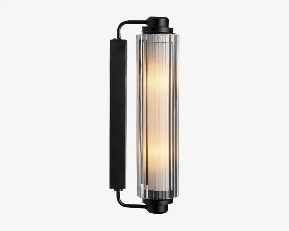 Væghængt lampe med cylindrisk glasskærm og lodrette rillede detaljer, der udsender et varmt lys. Lampen har en mat sort metalramme og endestykker, hvilket giver et moderne og industrielt udtryk. Designet er slankt og passer godt til nutidige indretninger.